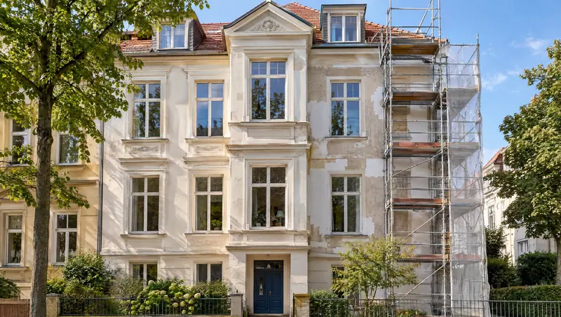 Älteres Wohnhaus mit Satteldach, dessen Fassade komplett eingerüstet ist, davor Baumaterial im Vorgarten